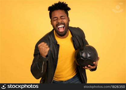 Portrait of an afro man celebrating victory while holding a football ball against an isolated background. Sports concept.