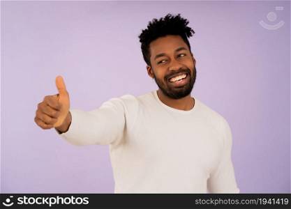 Portrait of an afro man showing thumbs up and smiling while standing against an isolated background.