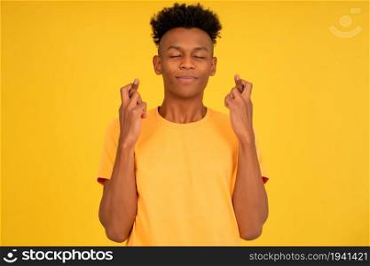 Portrait of an afro young man crossing her fingers wishing good luck while standing against an isolated background.