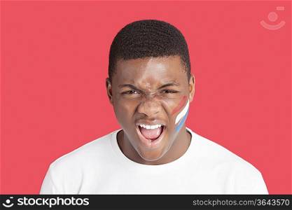 Portrait of an aggressive young man with Dutch flag on his face over red background