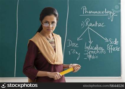 Portrait of an angry female lecturer holding ruler against green board