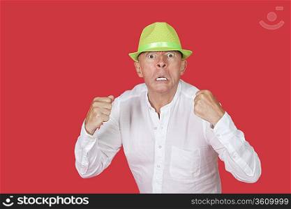 Portrait of an angry senior man clenching fists against red background