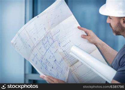 Portrait of an architect builder studying layout plan of the rooms, serious civil engineer working with documents on construction site, building and home renovation, professional foreman at work