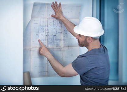 Portrait of an architect builder studying layout plan of the rooms, serious civil engineer working with documents on construction site, building and home renovation, professional foreman at work