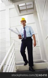 Portrait of an architect walking down stairs and carrying blueprints