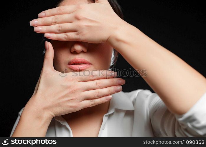 portrait of an Asian brunette woman in a white shirt covering her face with her hand on a black background