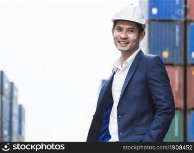 Portrait of an asian engineer wearing safety helmet with blur background of industrial containers.