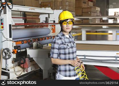 Portrait of an Asian female industrial worker with holding wire with machinery in background