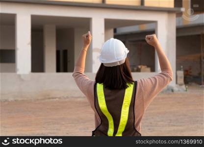Portrait of an Asian woman engineer construction worker wearing a helmet using a tablet while standing at a construction site. Building Location on the background, Concept of Equality and success