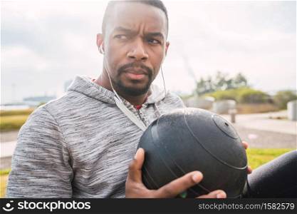 Portrait of an athletic man doing abdominal exercise with medicine ball in the park outdoors. Sport and healthy lifestyle.