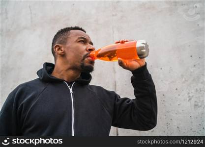 Portrait of an athletic man drinking something after training against grey background. Sport and health lifestyle.