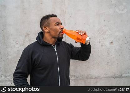 Portrait of an athletic man drinking something after training against grey background. Sport and health lifestyle.