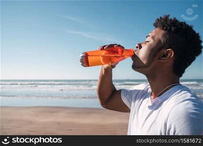 Portrait of an athletic man drinking something after training at the beach. Sport and health lifestyle.