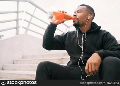 Portrait of an athletic man drinking something after training while sitting on concrete stairs. Sport and health lifestyle.