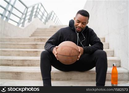 Portrait of an athletic man holding a basket ball while sitting on concrete stairs. Sport concept.
