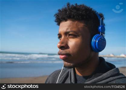 Portrait of an athletic man listening to music with earphones while resting for exercise at the beach. Sport and healthy lifestyle.