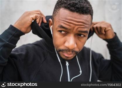 Portrait of an athletic man listening to music with earphones while resting for exercise, against grey background. Sport and healthy lifestyle.