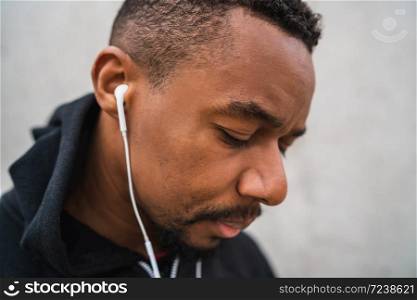 Portrait of an athletic man listening to music with earphones while resting for exercise, against grey background. Sport and healthy lifestyle.