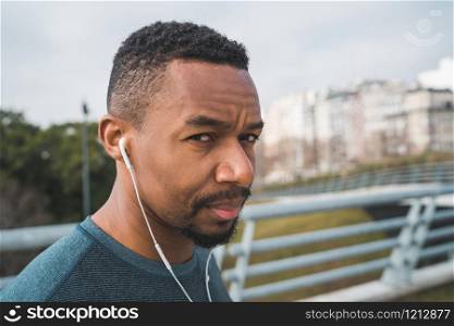 Portrait of an athletic man listening to music with earphones while resting for exercise outdoors. Sport and healthy lifestyle.