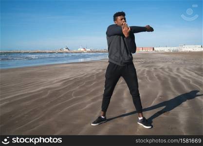 Portrait of an athletic man stretching arms before exercise at the beach. Sport and healthy lifestyle.