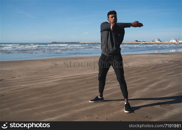 Portrait of an athletic man stretching arms before exercise at the beach. Sport and healthy lifestyle.