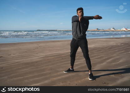 Portrait of an athletic man stretching arms before exercise at the beach. Sport and healthy lifestyle.