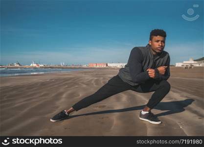Portrait of an athletic man stretching legs before exercise at the beach. Sport and healthy lifestyle.