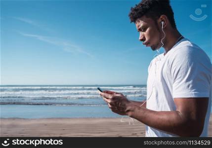 Portrait of an athletic man using his mobile phone on a break from training on the beach. Sport and health lifestyle.