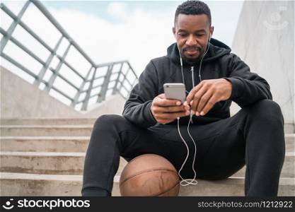 Portrait of an athletic man using his mobile phone on a break from training while sitting on concrete stairs. Sport and health concept.