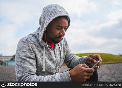 Portrait of an athletic man using his mobile phone on a break from training while sitting outdoors. Sport and health lifestyle.