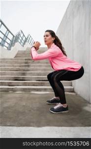 Portrait of an athletic woman doing exercise against grey wall. Sport and healthy lifestyle concept.