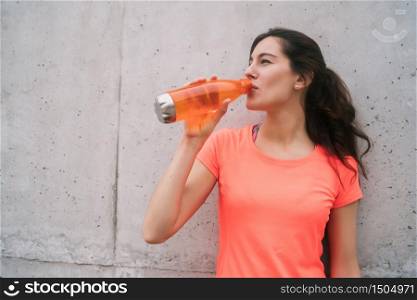 Portrait of an athletic woman drinking water after training against grey background. Sport and health lifestyle.