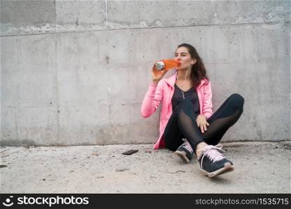 Portrait of an athletic woman drinking water after training against grey background. Sport and health lifestyle.