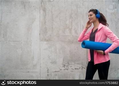 Portrait of an athletic woman holding a training mat while listening to music. Sport and lifestyle concept.