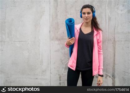 Portrait of an athletic woman holding a training mat while listening to music. Sport and lifestyle concept.
