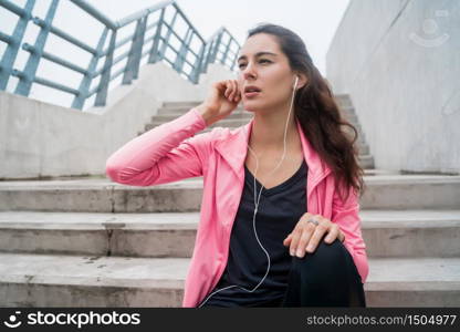 Portrait of an athletic woman listening to music on a break from training while sitting on stairs. Sport and health lifestyle concept.