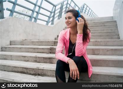 Portrait of an athletic woman listening to music on a break from training while sitting on stairs. Sport and health lifestyle concept.