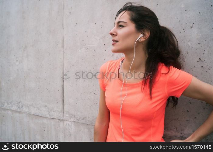 Portrait of an athletic woman listening to music on a break from training against grey background. Sport and health lifestyle.