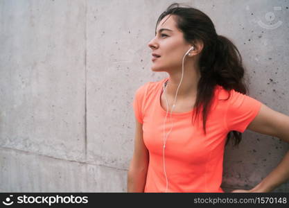 Portrait of an athletic woman listening to music on a break from training against grey background. Sport and health lifestyle.