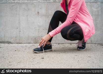 Portrait of an athletic woman tying her shoelaces and getting ready for jogging outdoors. Sport and healthy lifestyle concept.