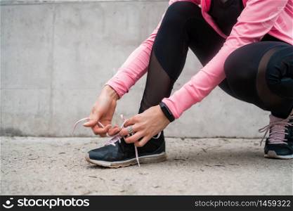 Portrait of an athletic woman tying her shoelaces and getting ready for jogging outdoors. Sport and healthy lifestyle concept.
