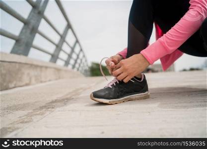 Portrait of an athletic woman tying her shoelaces and getting ready for jogging outdoors. Sport and healthy lifestyle concept.