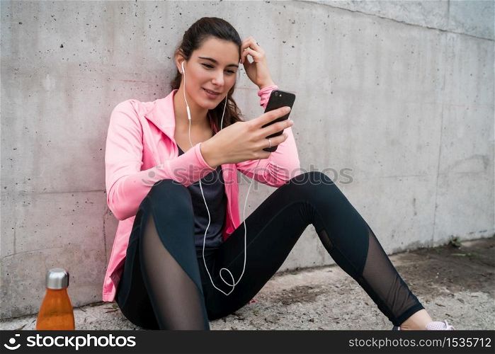 Portrait of an athletic woman using her mobile phone on a break from training against grey background. Sport and health lifestyle.