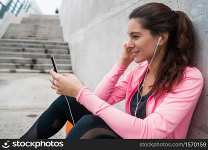 Portrait of an athletic woman using her mobile phone on a break from training against grey background. Sport and health lifestyle.
