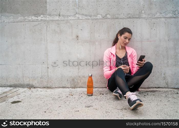 Portrait of an athletic woman using his mobile phone on a break from training against grey background. Sport and health lifestyle.