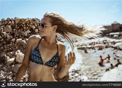 Portrait of an Attractive Blond Female on the Beach. Beautiful Model Posing over Stones Background. Happy Summer Vacation in Croatia. Europe.. Beautiful Woman on the Beach