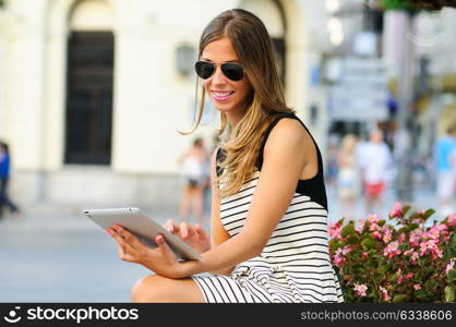 Portrait of an attractive blonde woman with tablet computer in urban background