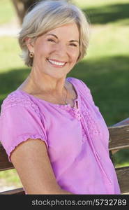 Portrait of an attractive elegant senior woman sitting outside with green grass behind her.