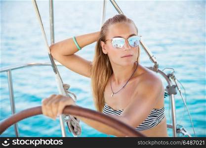 Portrait of an attractive girl on sailboat, wearing stylish sunglasses and bikini, luxury summer vacation on the sea, active holidays. Attractive girl on sailboat