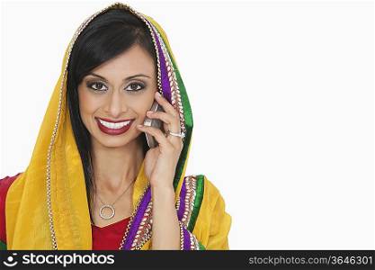 Portrait of an attractive Indian woman in traditional wear answering phone call over gray background